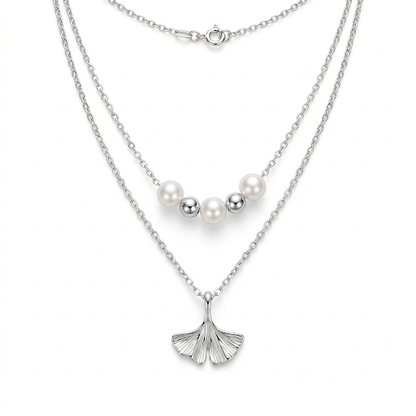 Two layered silver necklaces with pearl beads and a ginkgo leaf pendant on a white background.